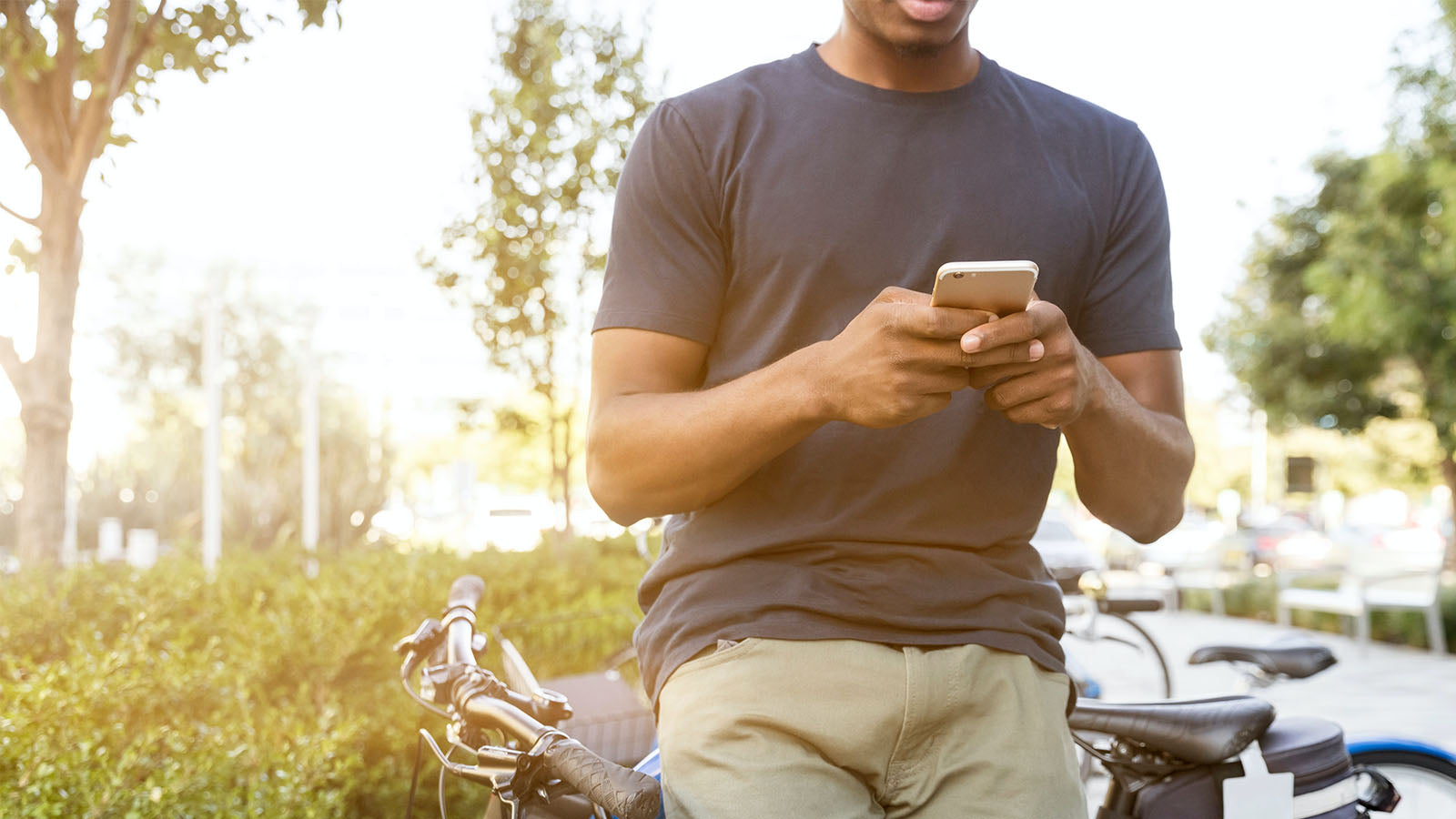 A man leaning against a bicycle outdoors, looking at his phone.
