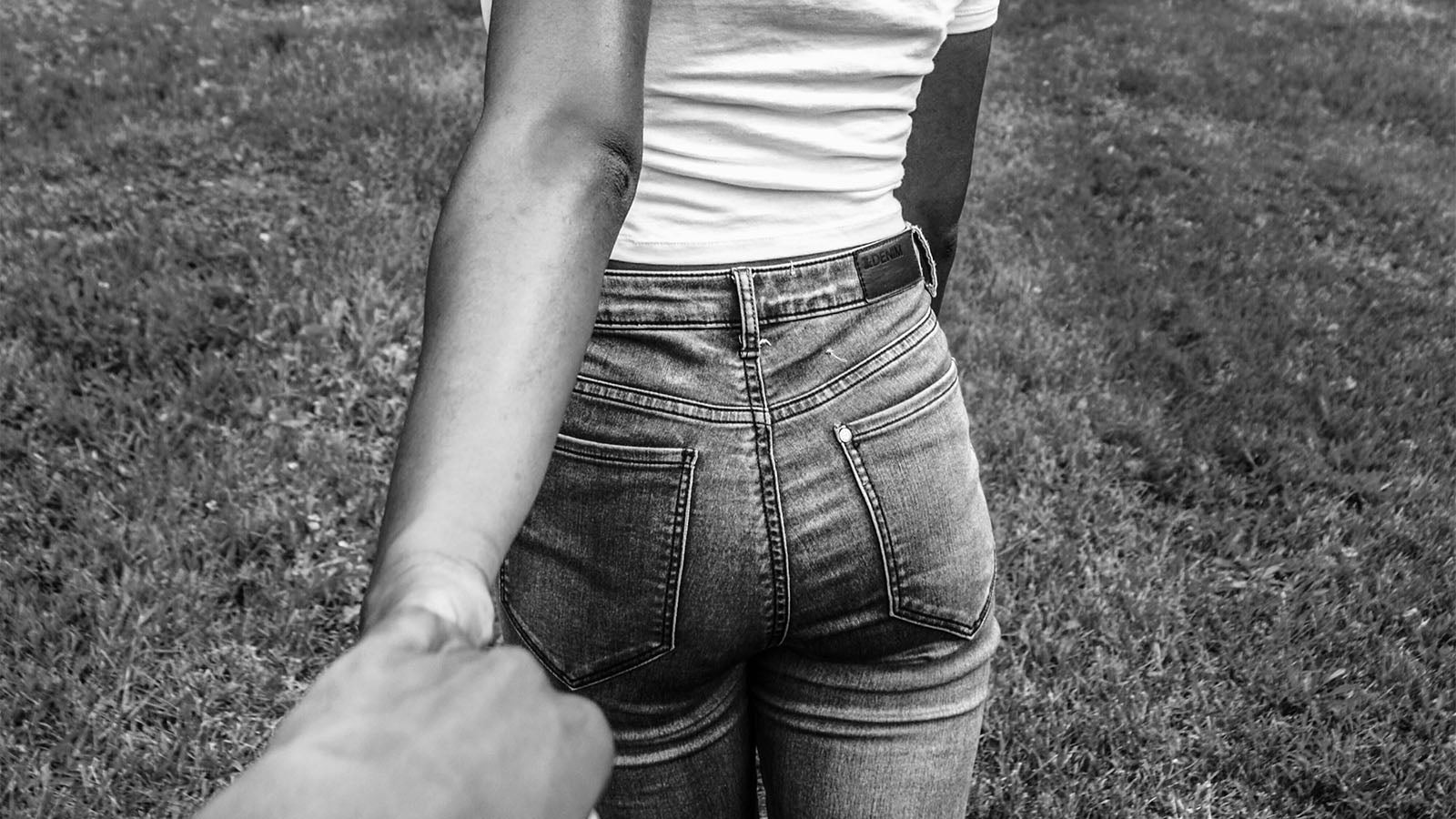 A black and white photograph of a woman leading someone by the hand across a lawn, seen from behind.