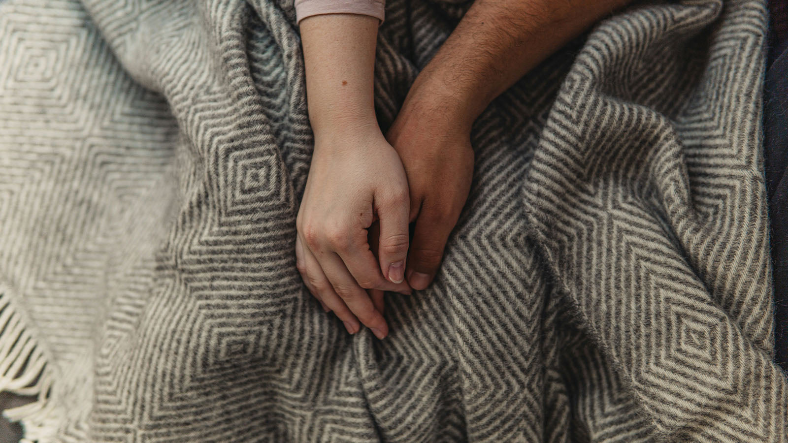 Two hands resting side by side on a woollen blanket, one reaching toward the other.