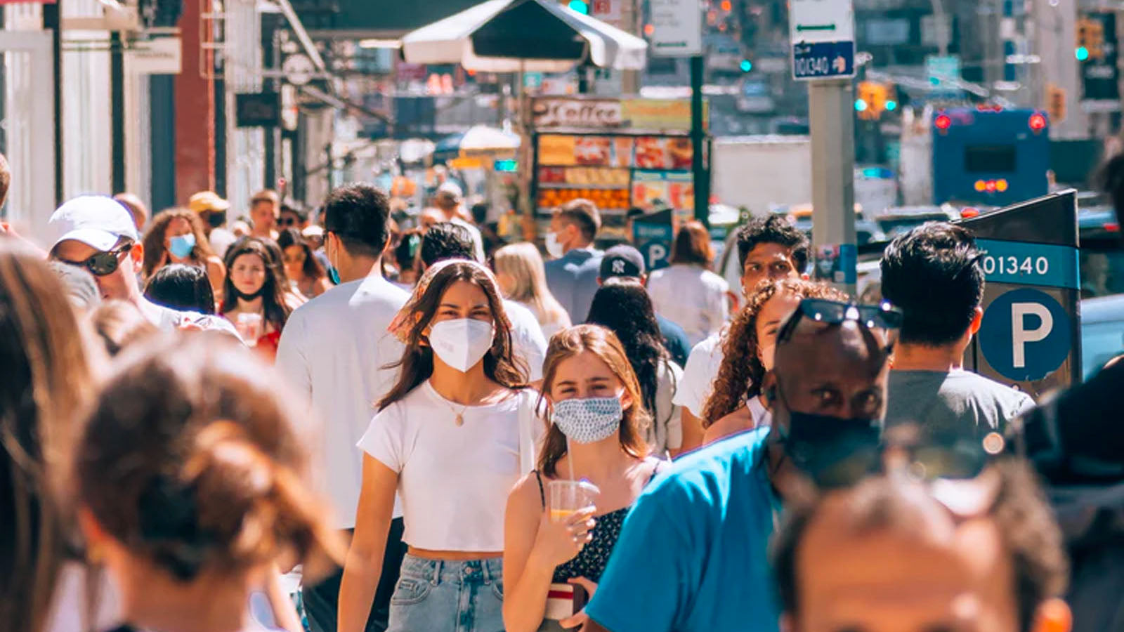 A crowded city street with many people wearing face masks.