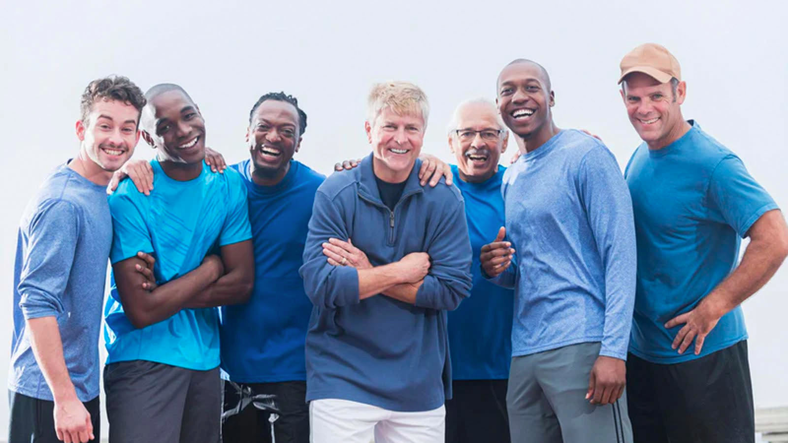 A group of seven men of different ages and ethnicities standing together in sportswear, smiling at the camera.