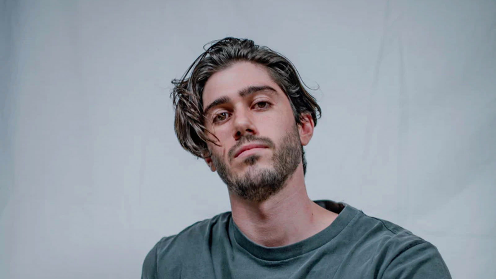 A young man with a beard looking directly at the camera against a plain grey backdrop.
