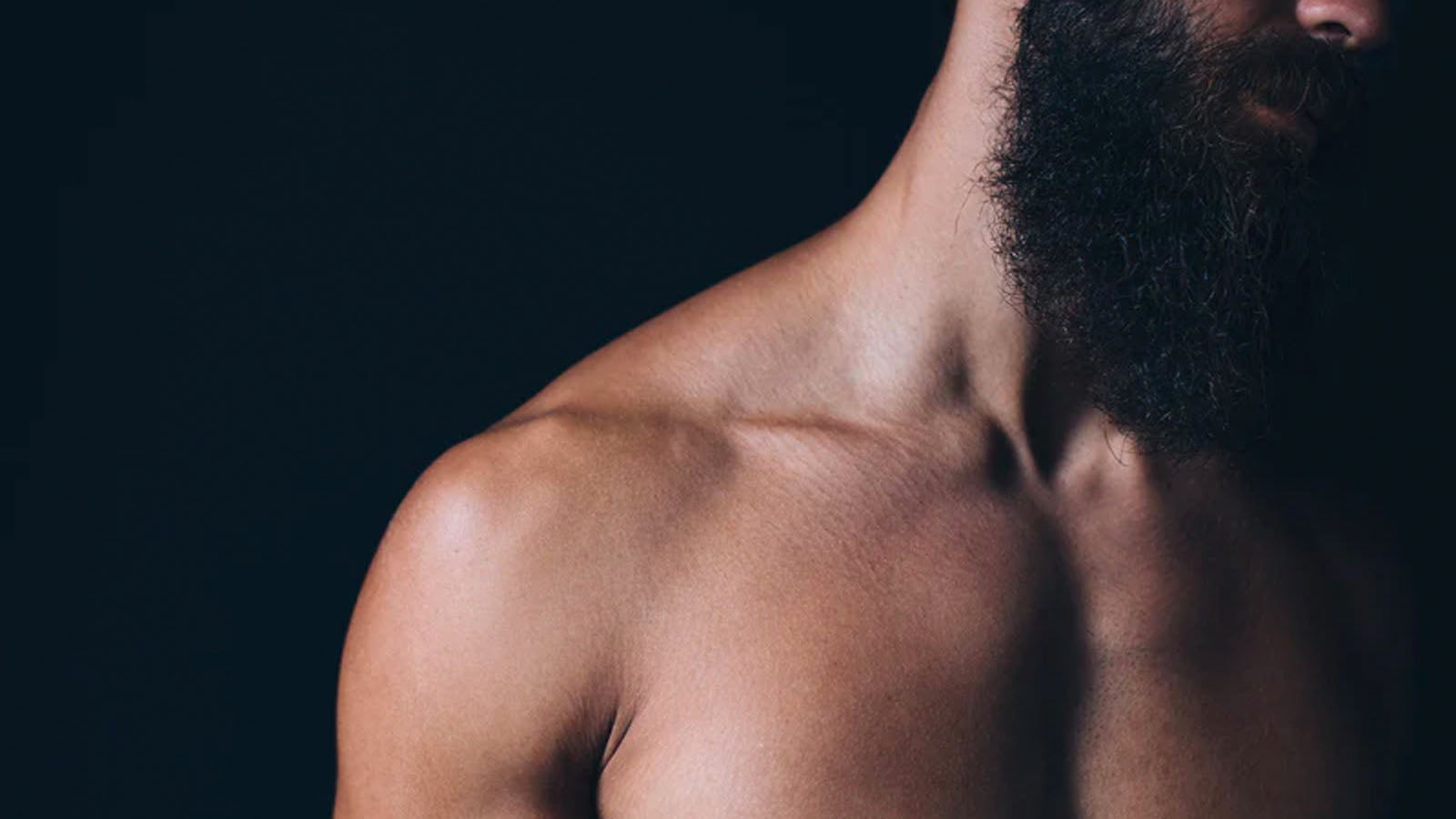 A close photograph of a bearded man's bare shoulder and neck against a dark background.