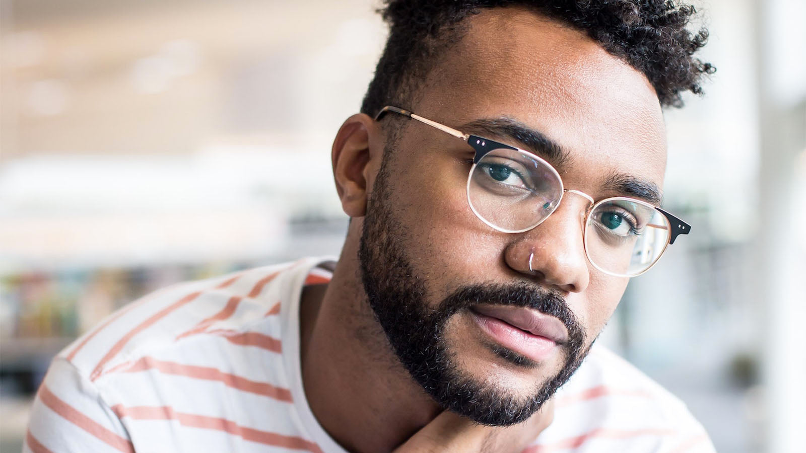 A close portrait of a man in glasses resting his chin on his hand, looking away from the camera.