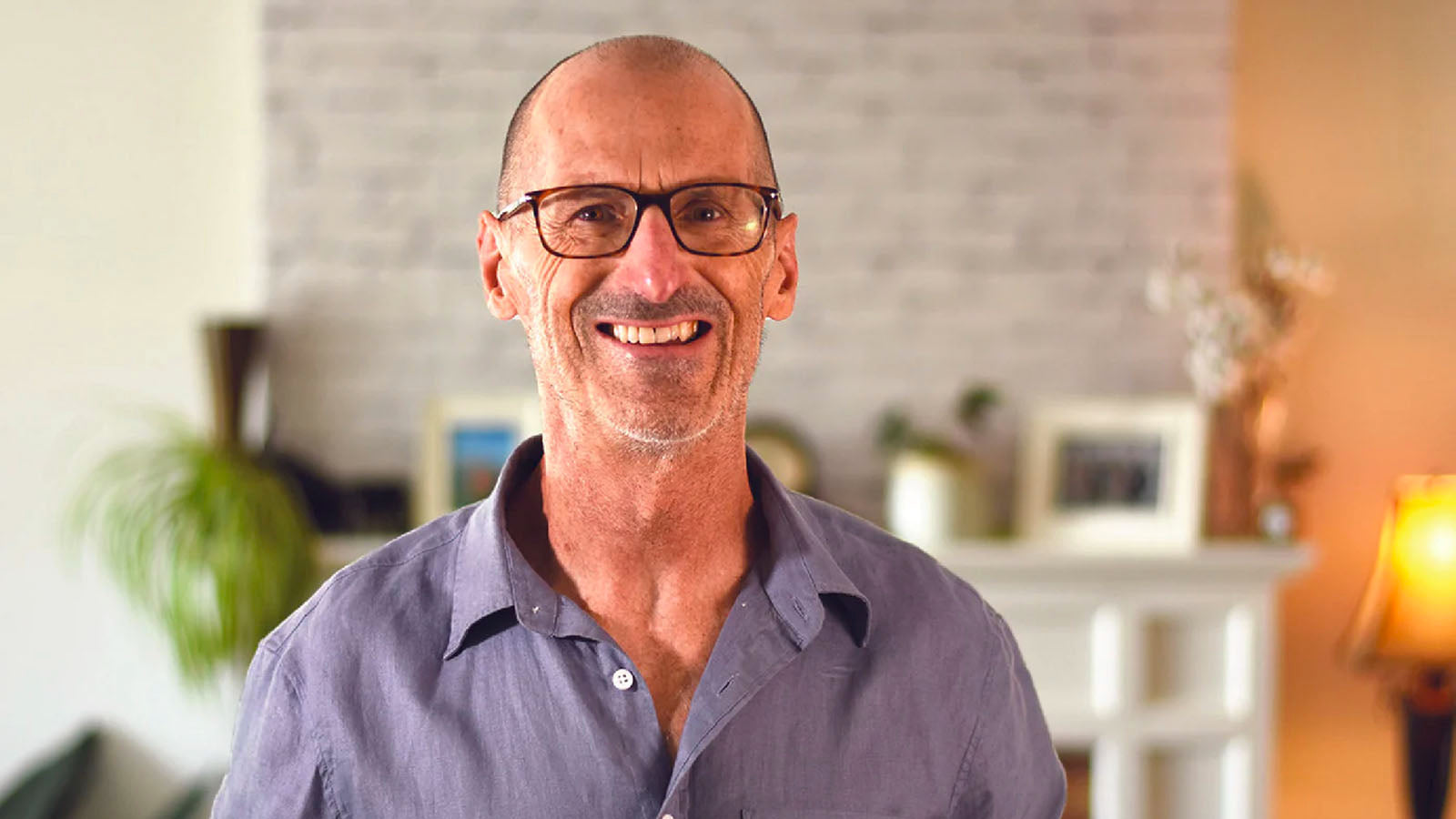 Nigel Shaw, founder and inventor of Xialla, smiling in a living room wearing glasses and a linen shirt.