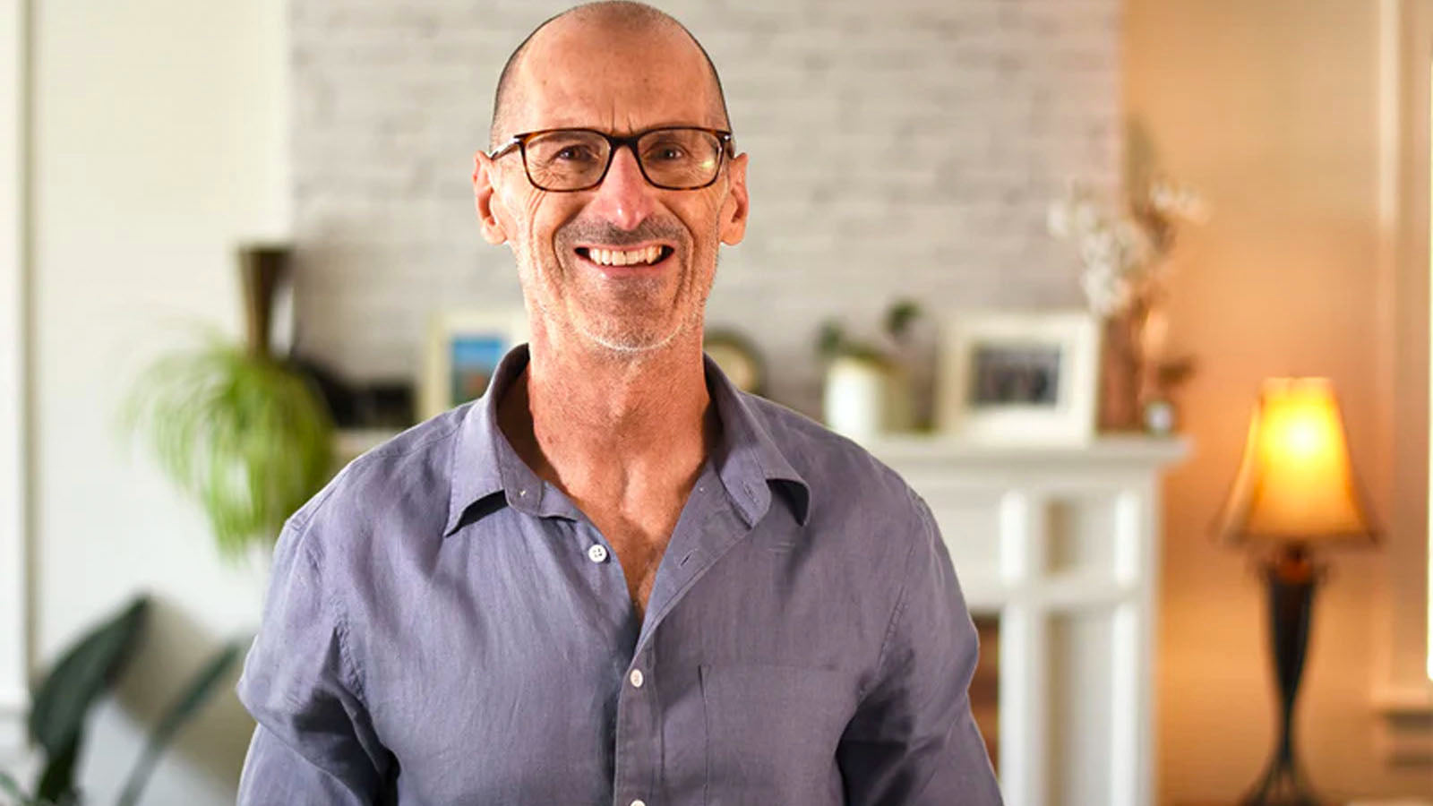 Nigel Shaw, inventor of Xialla, smiling in a living room wearing glasses and a linen shirt.