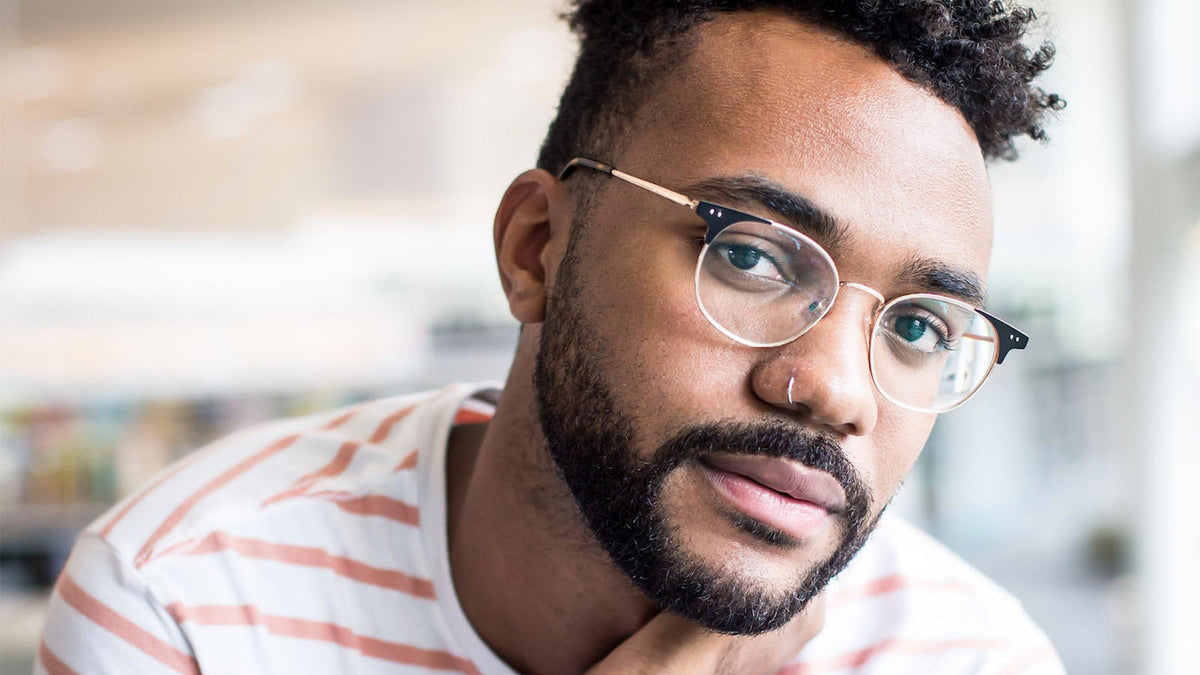 A close portrait of a man in glasses resting his chin on his hand, looking away from the camera.