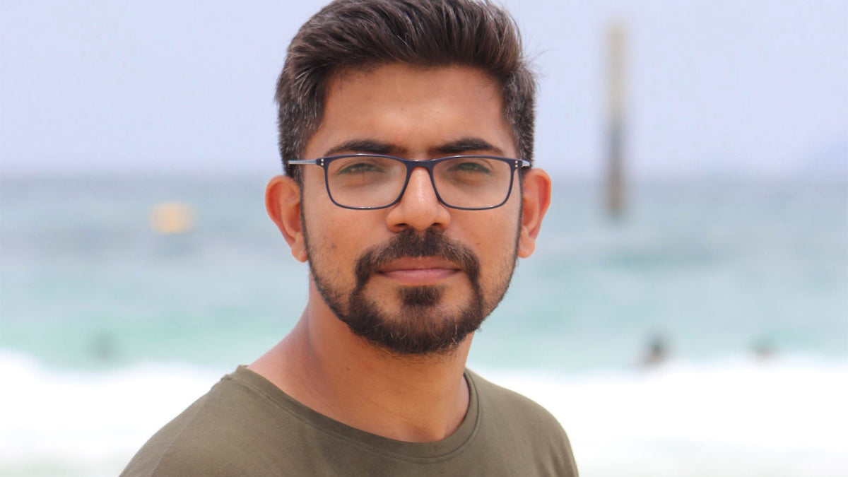 A man in glasses and an olive t-shirt looking at the camera, with the sea behind him.
